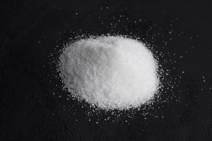 A small pile of white crystalline powder on a dark surface, highlighting its texture and purity, commonly associated with salt or chemical compounds.